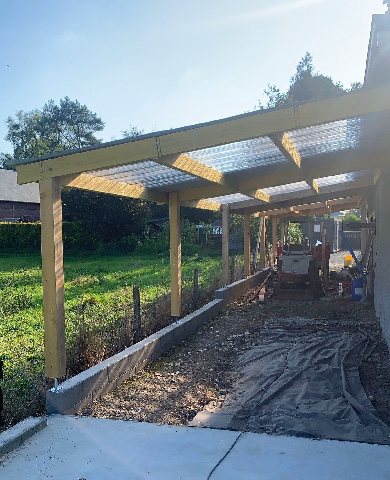 Abri de voiture en bois en construction ; panneaux de toiture translucides.
