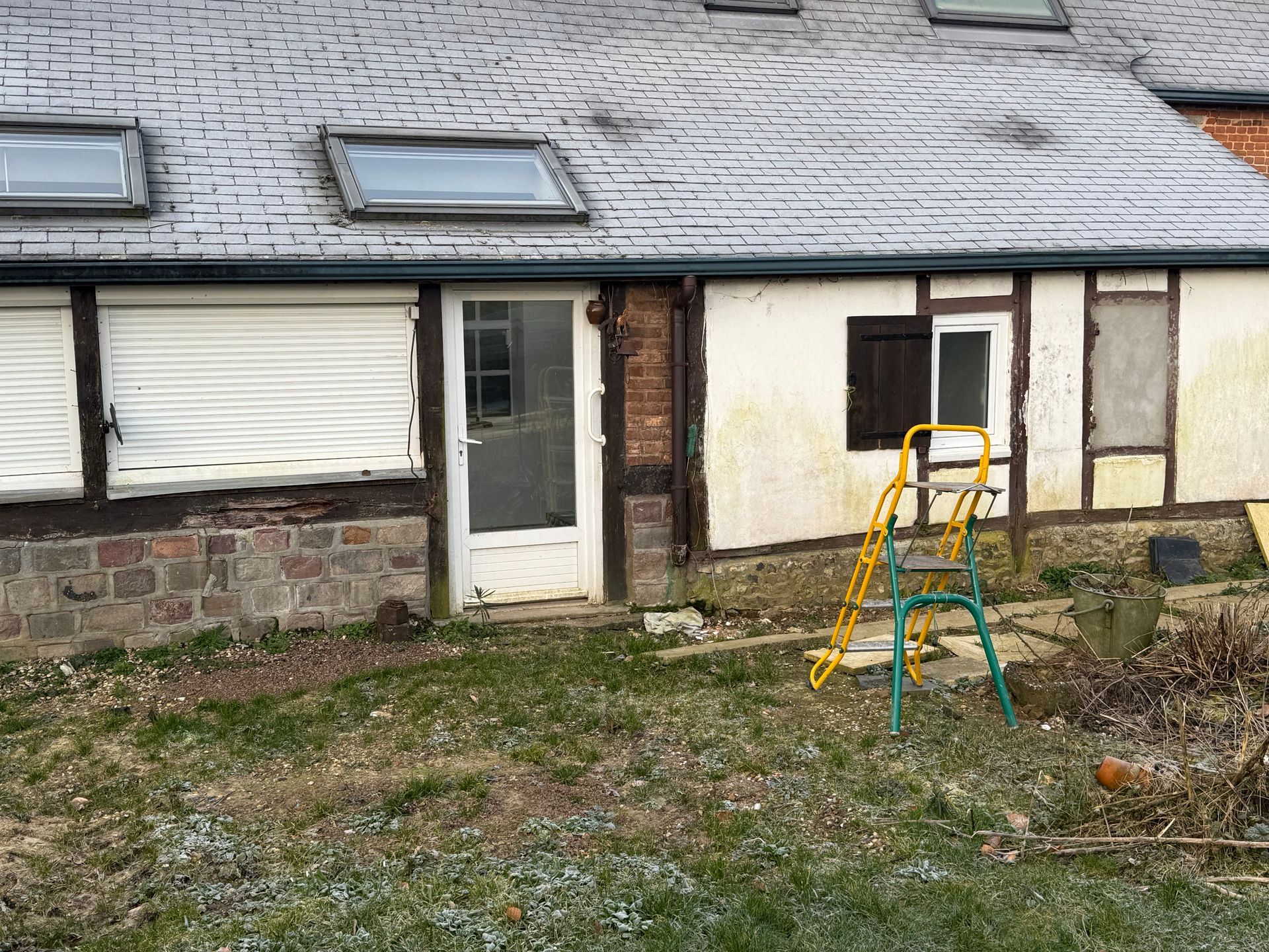 Extérieur d'un bâtiment avec une porte blanche, des fenêtres et une échelle sur la pelouse devant.