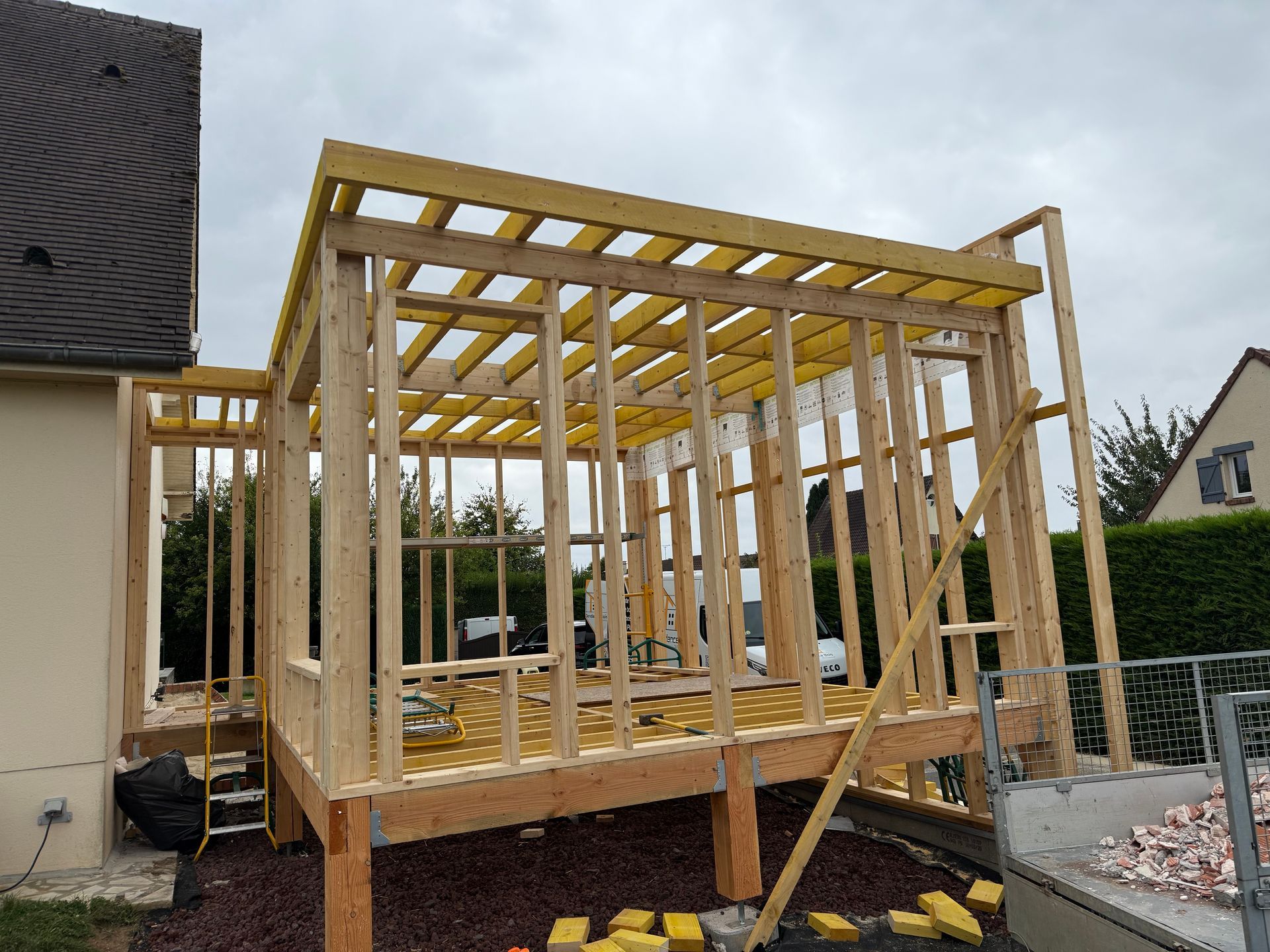 Structure à ossature en bois d'un bâtiment en construction, vue extérieure. Bois jaune, ciel nuageux, herbe verte.