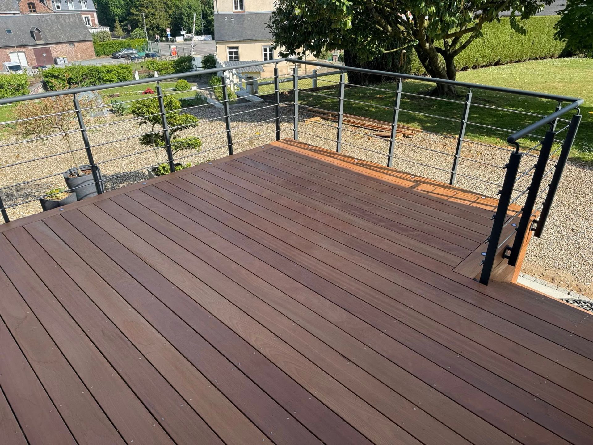 Terrasse en bois avec rambarde en métal donnant sur une cour.
