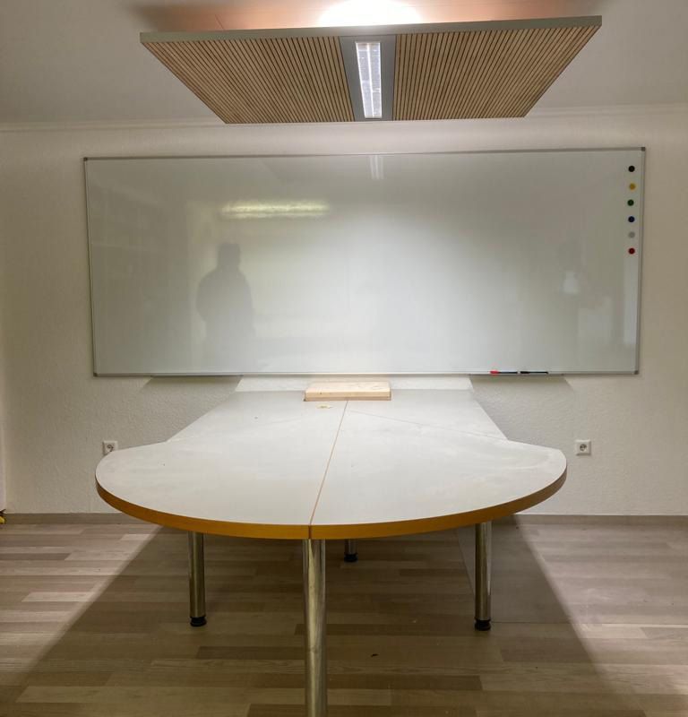Ein Konferenztisch mit rundem Ende und eine Holztafel mit Beleuchtung an der Decke
