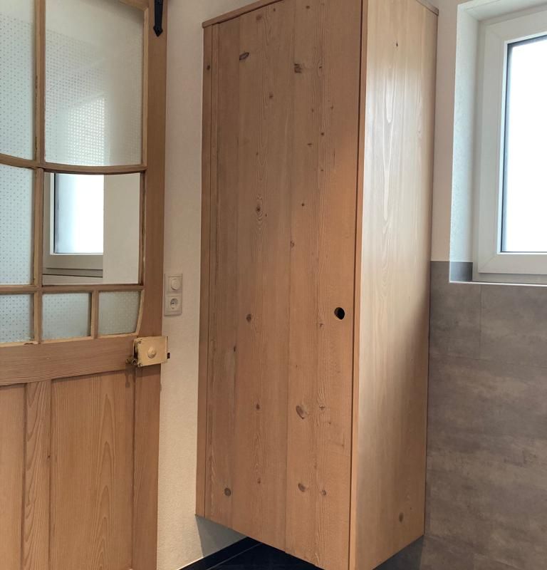 ein hängender Holzschrank neben einer Holztür und einem Fenster