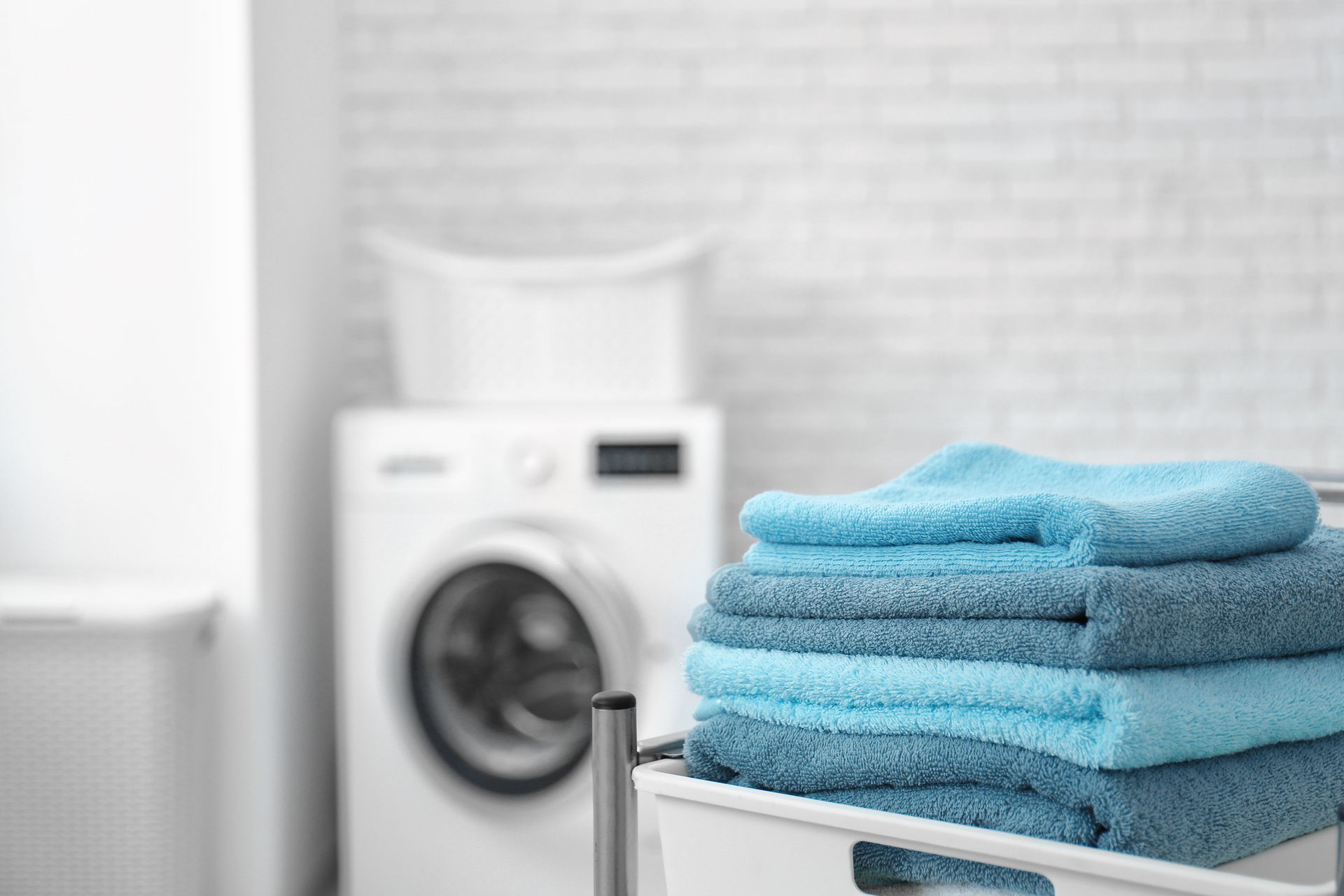 Des serviettes bleues empilées dans une buanderie avec une machine à laver en arrière-plan