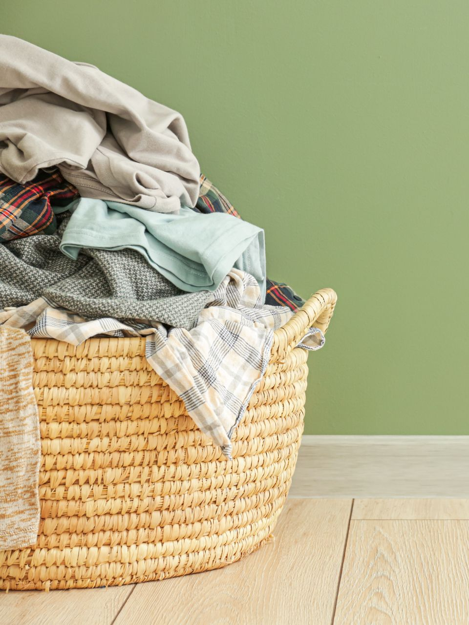 Du linge dans un panier en osier sur un parquet clair, contre un mur vert pâle.