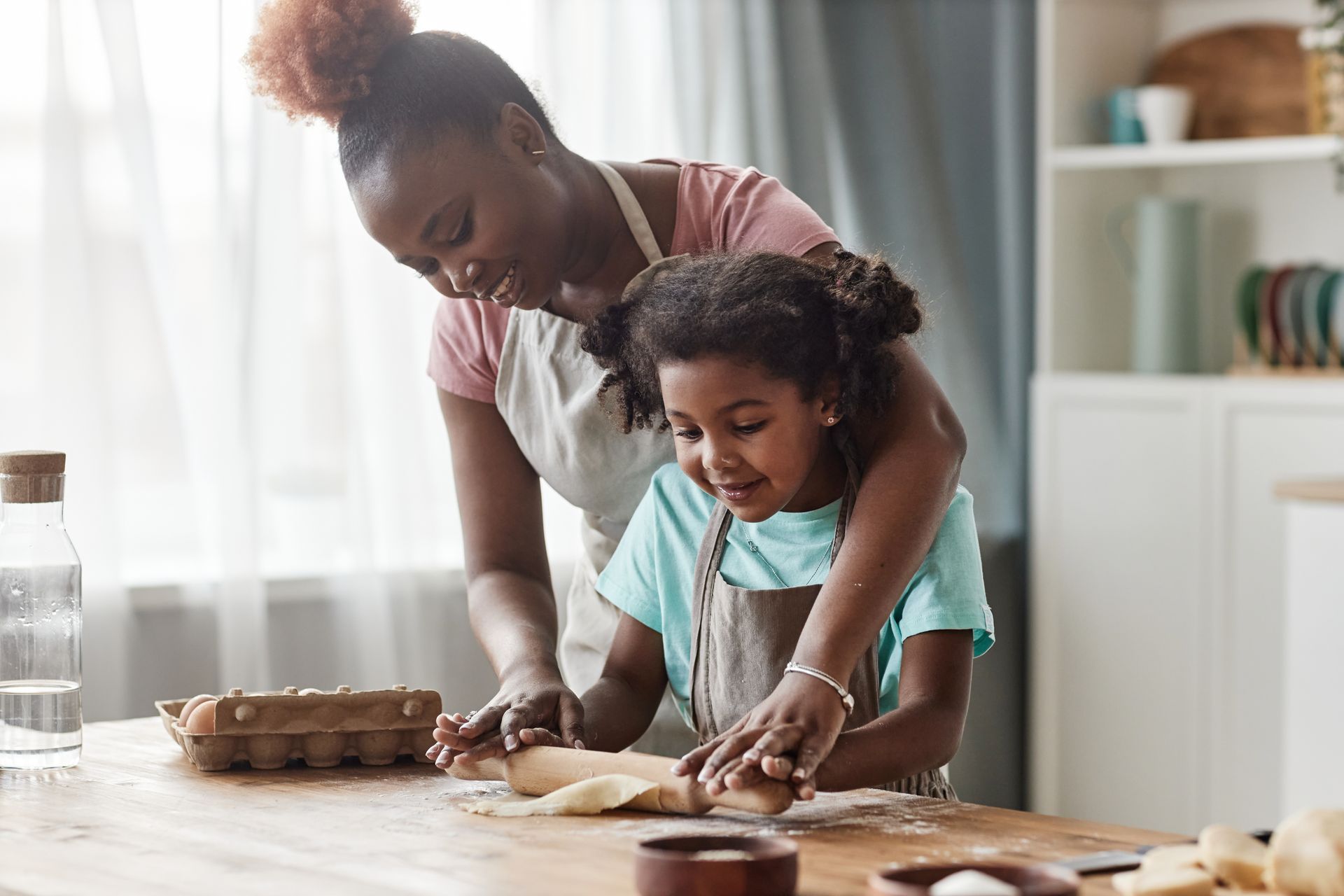 Un adulte et un enfant font de la pâtisserie ensemble sur le plan de travail de la cuisine, étalant la pâte avec de la farine et des ustensiles à proximité.