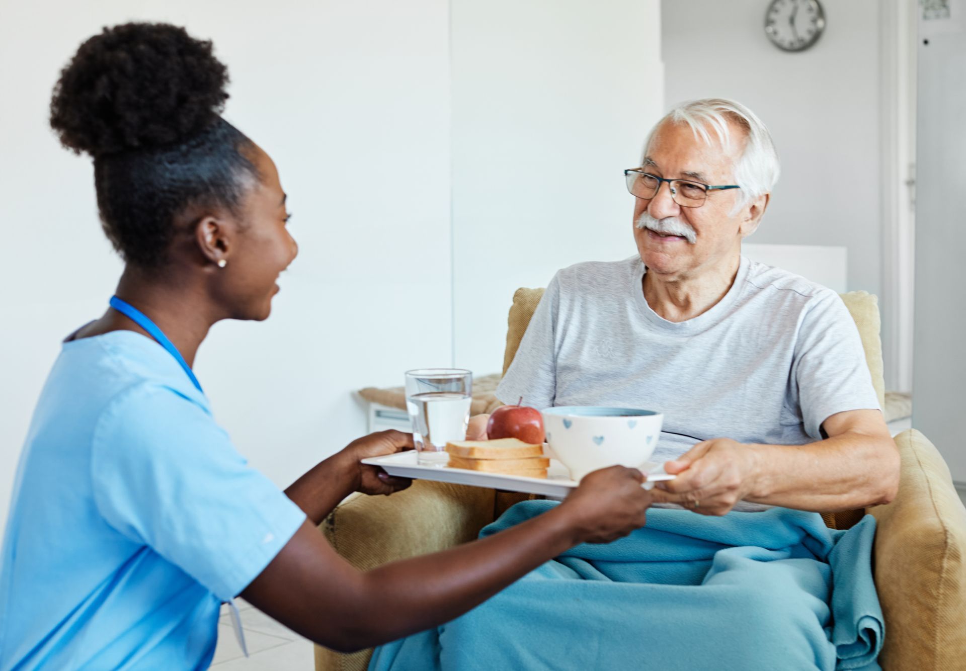 Une infirmière sert le petit-déjeuner à un patient souriant, assis dans son lit avec un plateau et une tasse d'eau.