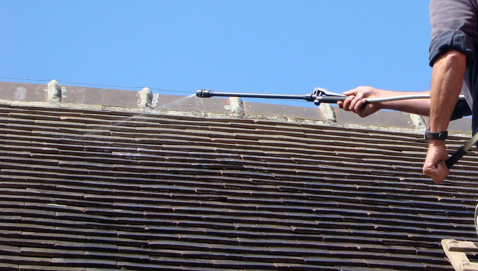 Focus sur un homme qui passe un produit pour démousser une toiture en ardoise