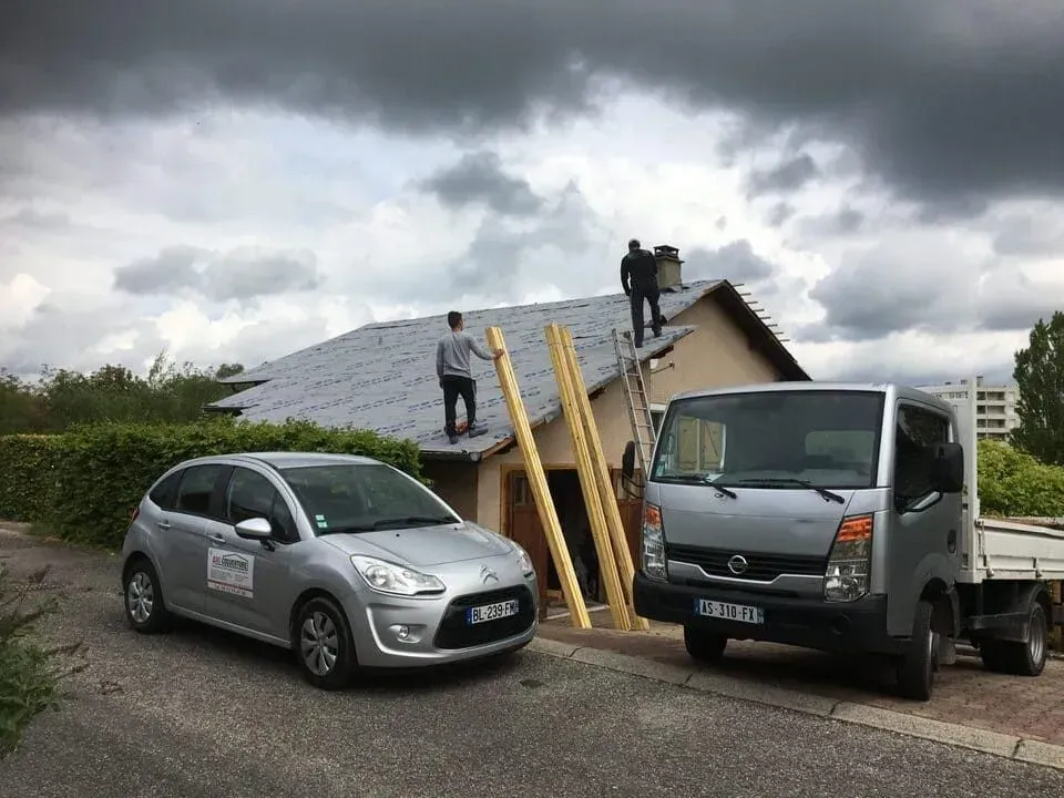 Deux ouvriers sur un toit en construction avec deux véhicules de l'entreprise