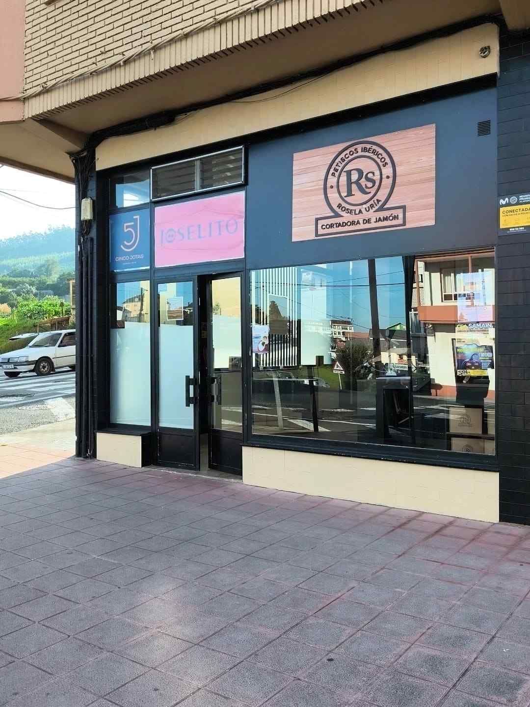 Fachada de tienda con escaparates de cristal, carteles y puerta a acera.