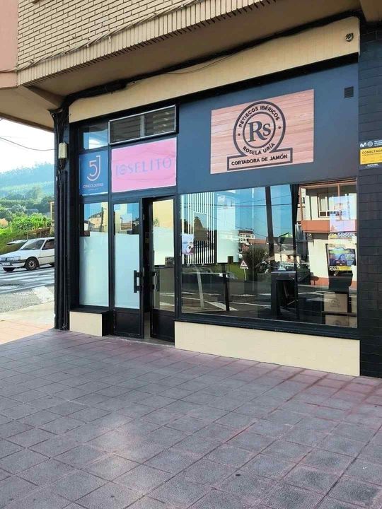 Fachada de tienda con escaparates de cristal, carteles y puerta a acera.