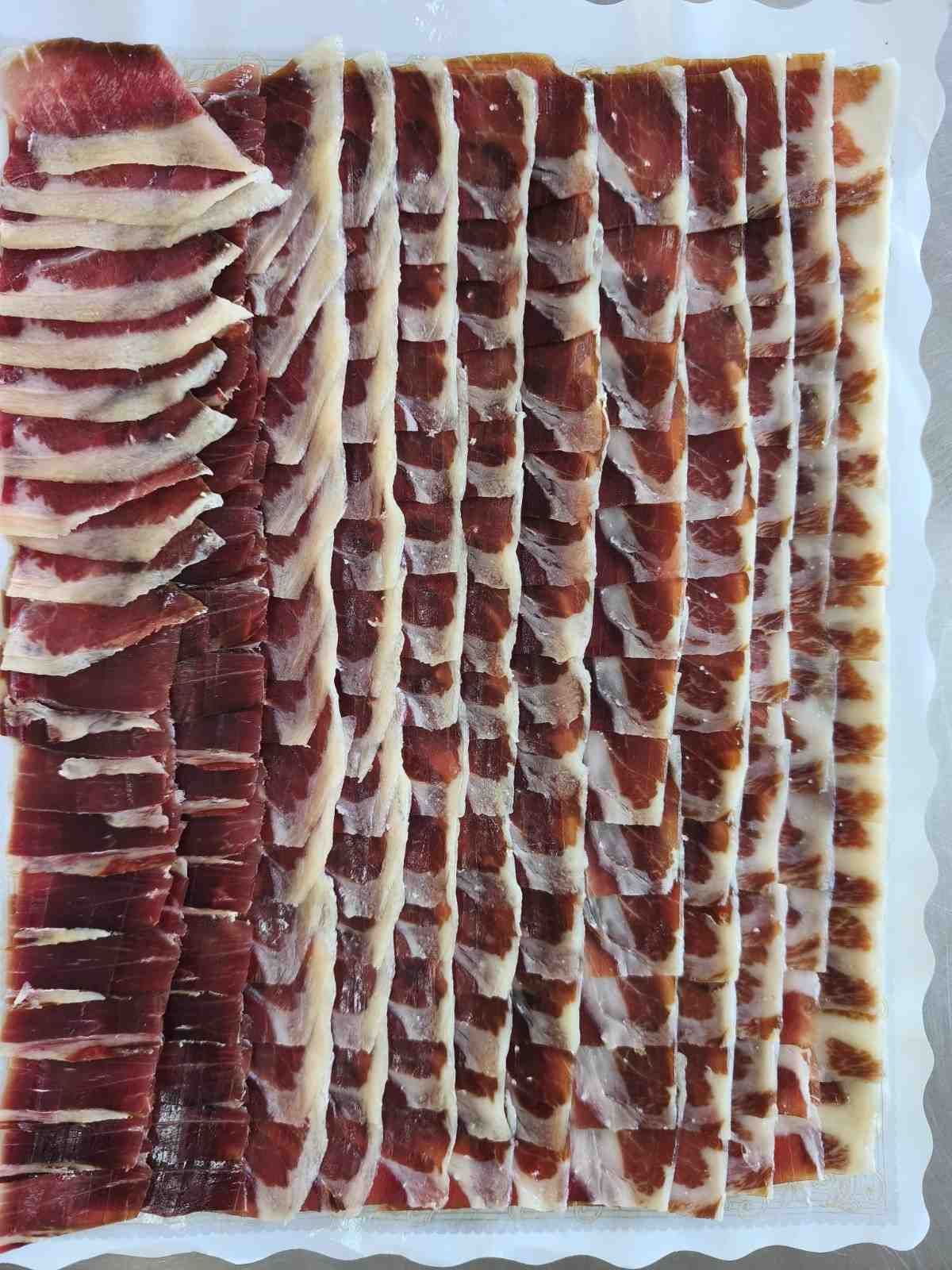 Jamón ibérico de bellota cortado fino y dispuesto en recipiente blanco, mostrando vetas rojas y blancas.