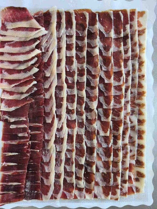 Jamón ibérico de bellota cortado fino y dispuesto en recipiente blanco, mostrando vetas rojas y blancas.