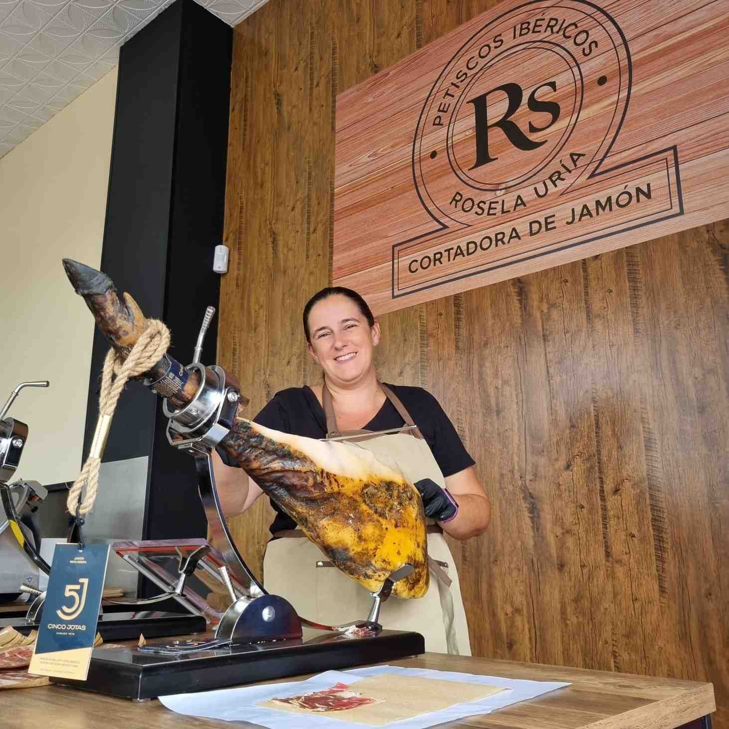 Mujer con pata de jamón, sonriendo detrás de un mostrador con un cartel 