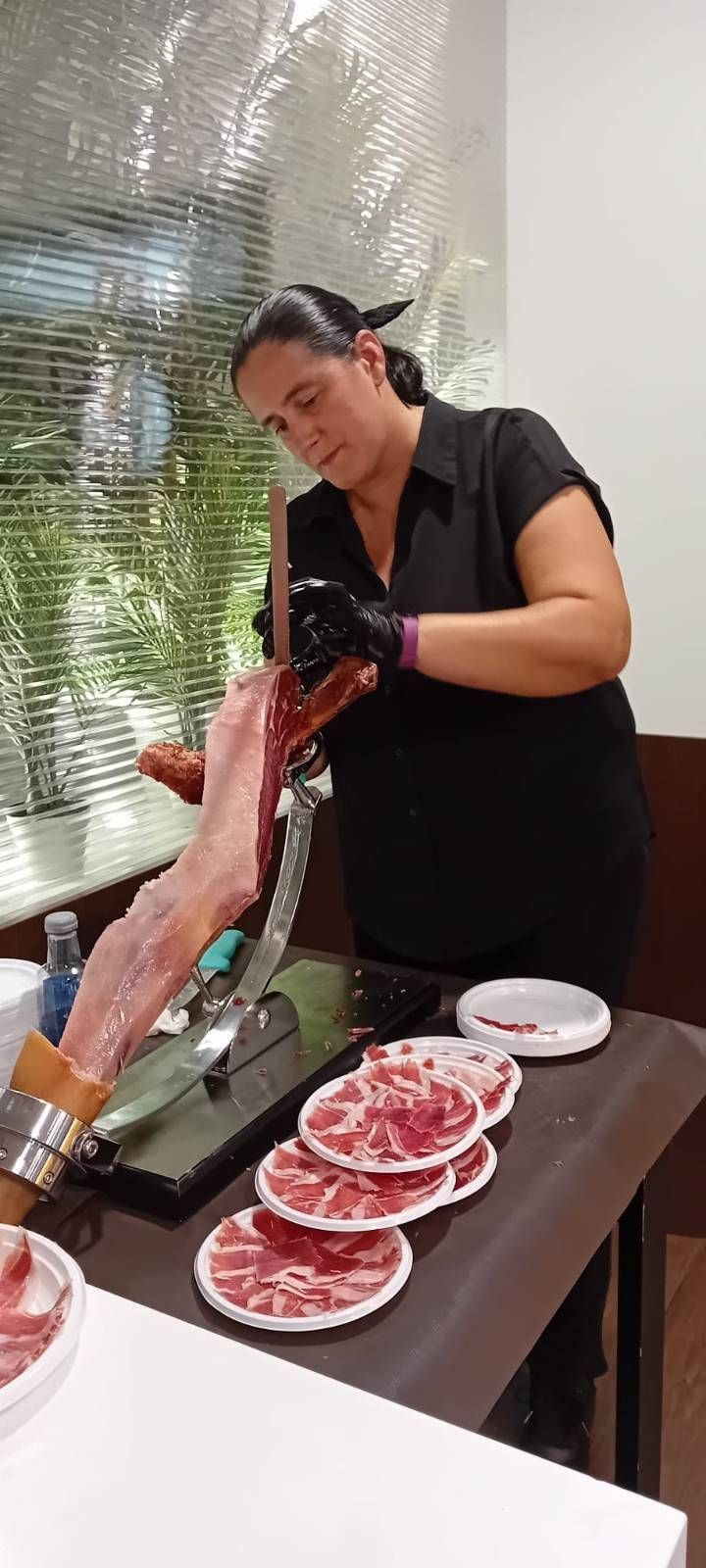 Una persona corta jamón en una mesa con rodajas de jamón ya dispuestas en pequeños platos blancos.