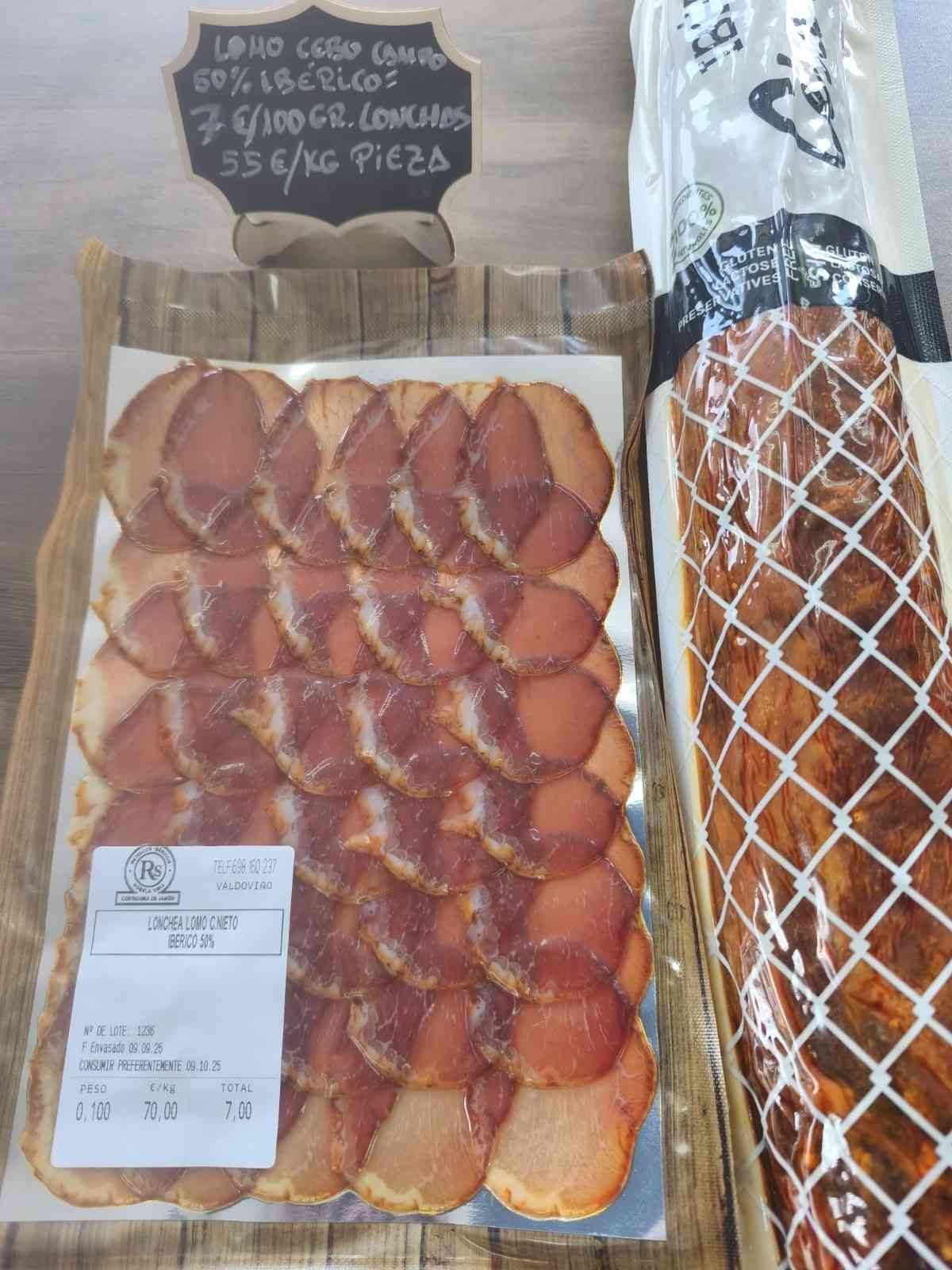 Cerdo curado en lonchas, envasado para la venta, junto con una pieza entera. Un cartel manuscrito indica el precio.