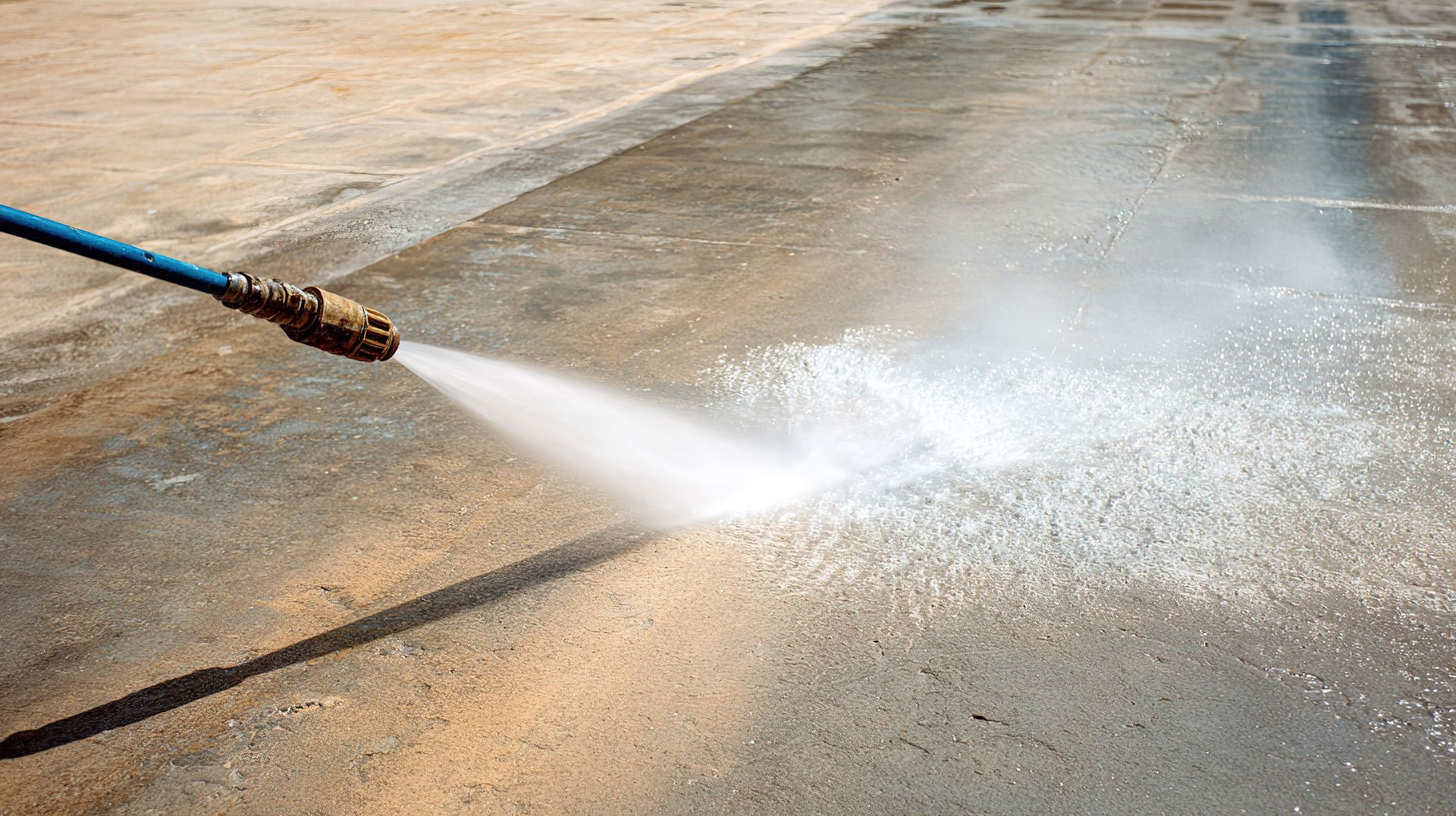 Un tuyau d'arrosage projette de l'eau sur une surface en béton, créant ainsi une brume.
