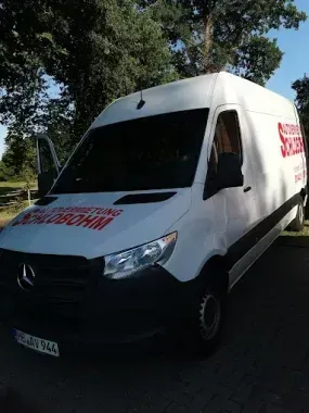 Ein weißer Mercedes-Lieferwagen mit roter Aufschrift an der Seite parkt im Sonnenlicht.