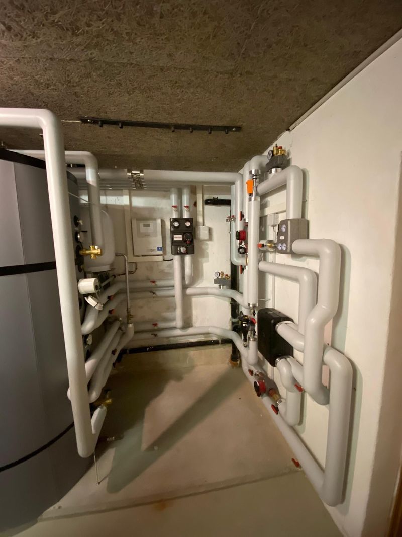 Rohre und Ventile in einem Betonraum. Isolierte Rohre verlaufen an der Decke. Rote und blaue Ventilgriffe.