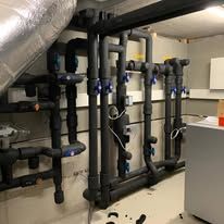 Weisse Rohre und Manometer für eine Heizungsanlage im Keller.