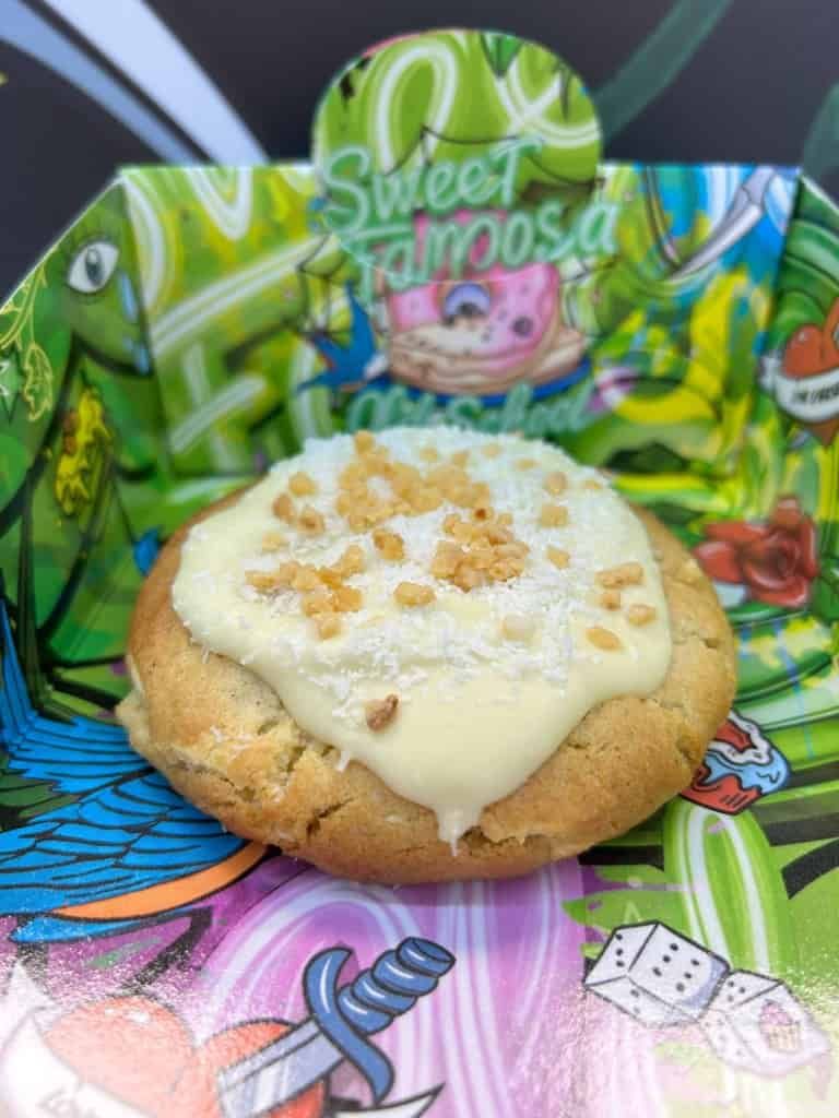 Una galleta con glaseado blanco y chispas en una colorida caja de la marca Sweet Tattoos.