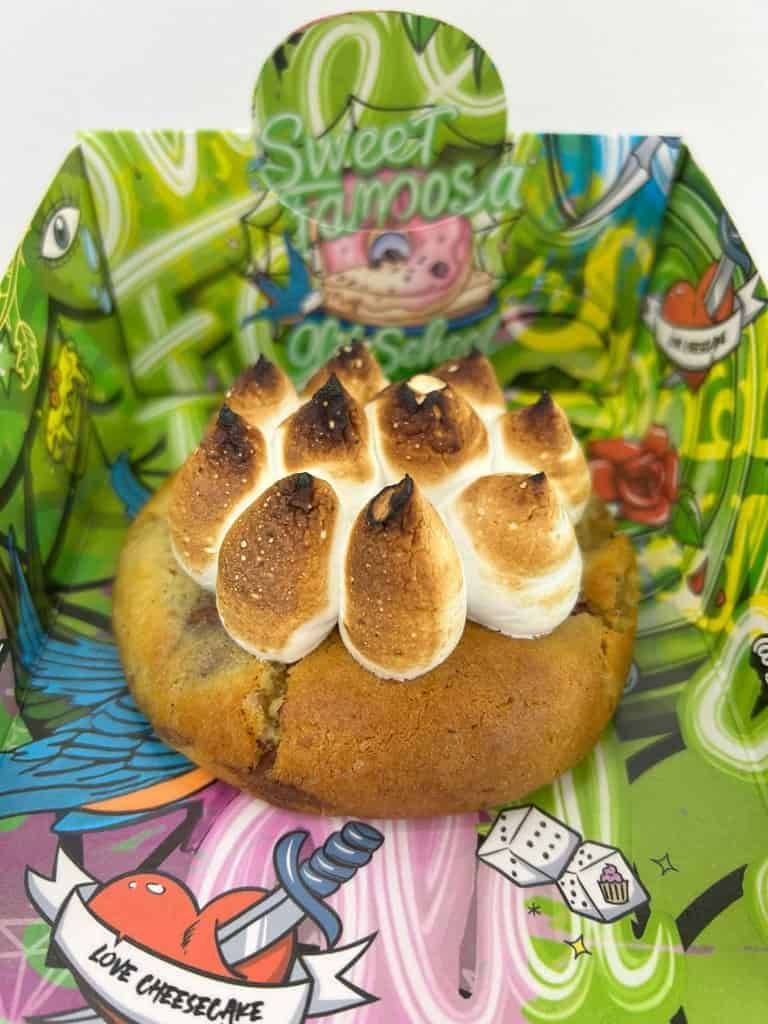 Galleta cubierta con malvavisco tostado, ubicada en un recipiente colorido con arte estilo grafiti y una pancarta que dice