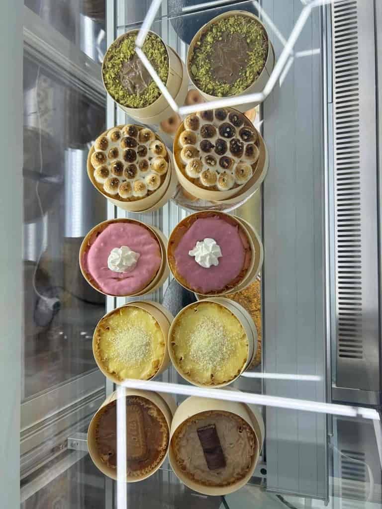 Vitrina llena de pasteles redondos individuales, de distintos sabores y aderezos como nueces, merengue y crema, dentro de una cafetería.