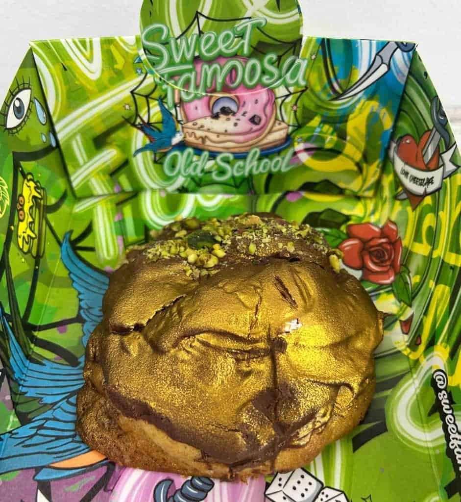 Pastel cubierto de oro con cobertura de pistacho en un recipiente con estampado verde y el logo