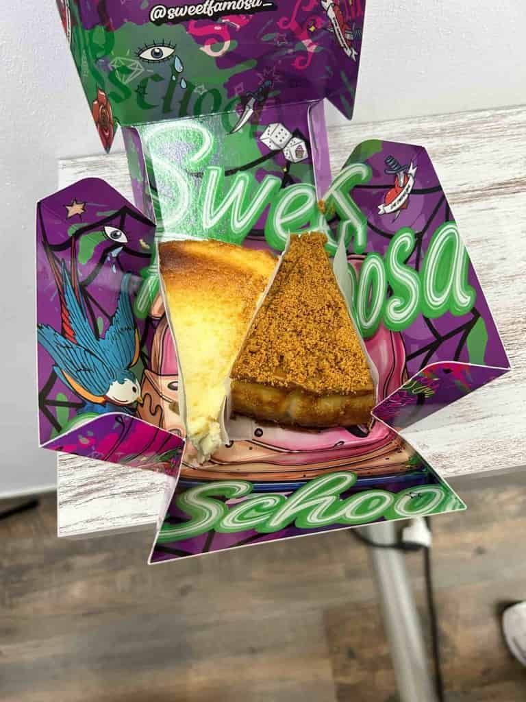 Rebanadas de tarta de queso en una colorida caja de la escuela Sweet Rosa. La caja es morada y verde con diseños artísticos.