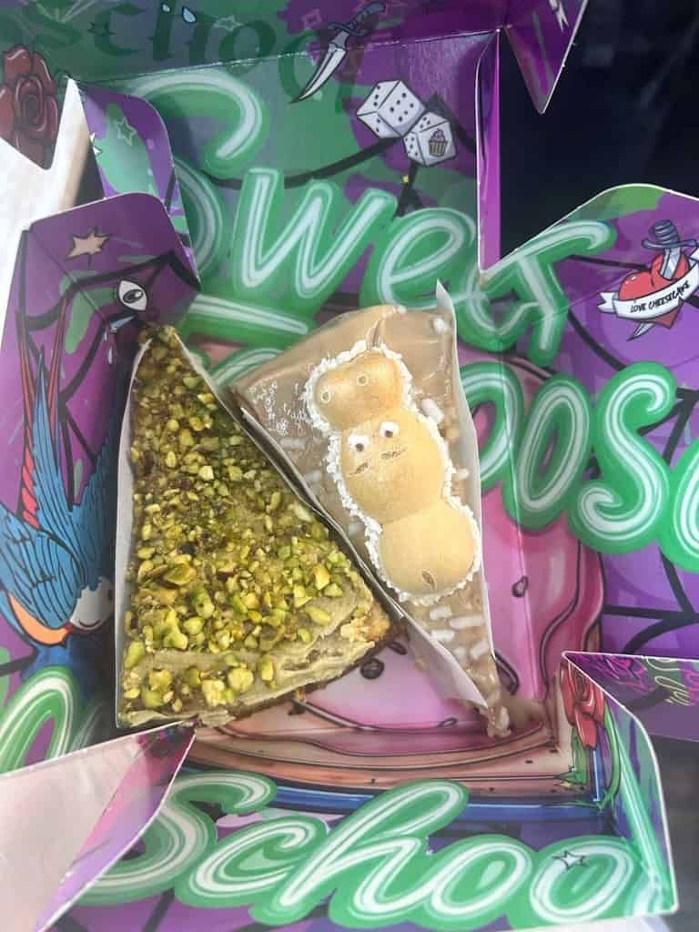 Dos rebanadas de pastel de postre, una cubierta de pistacho y la otra con un osito de malvavisco, en una caja colorida con gráficos de