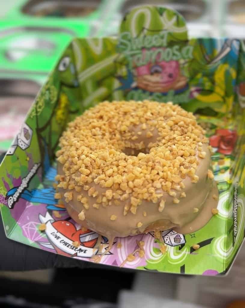 Una dona con glaseado de caramelo y maní se encuentra en un recipiente de cartón decorado y colorido.