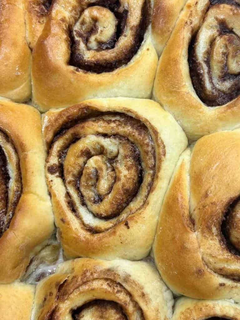 Primer plano de rollos de canela recién horneados, de color marrón dorado con capas visibles y remolinos de relleno de canela.