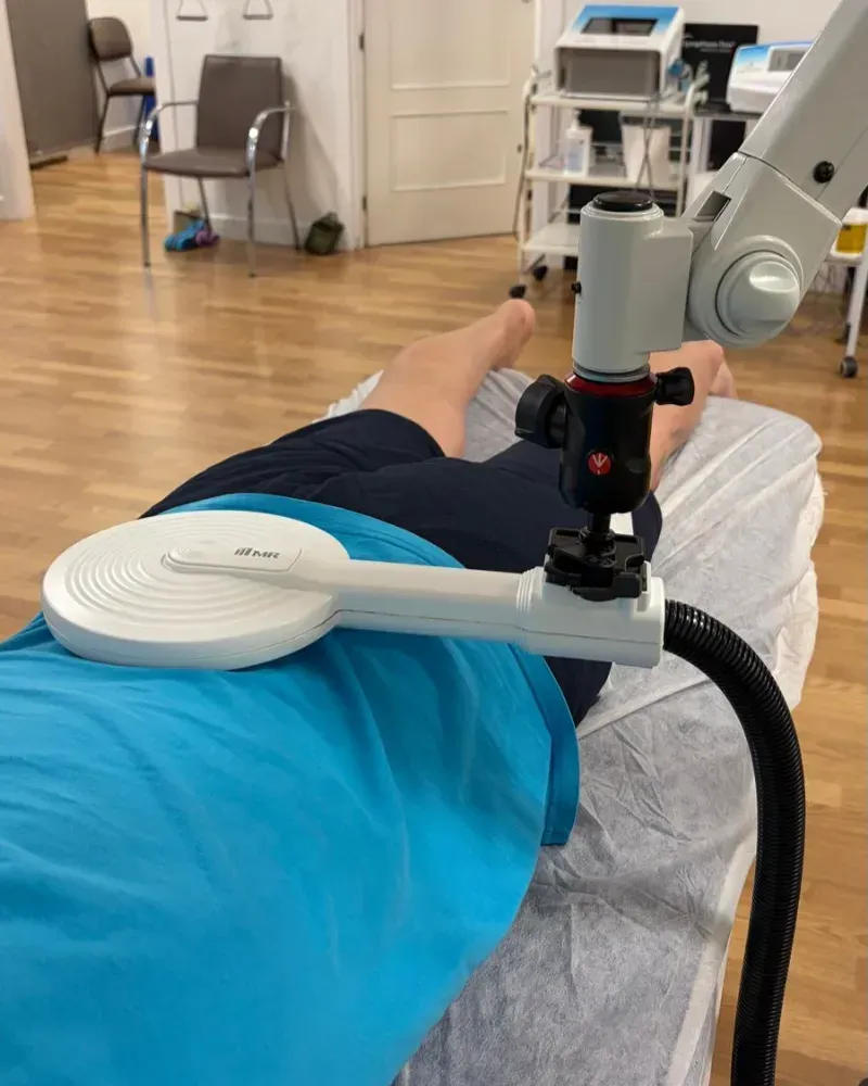 Un fisioterapeuta le da un masaje en el hombro a un paciente sentado en una sala de consulta.