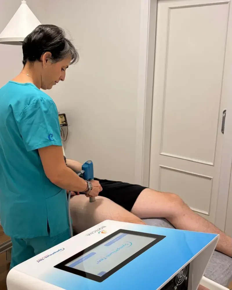 Una médica con bata blanca se encuentra en una clínica luminosa, sonriendo amablemente.
