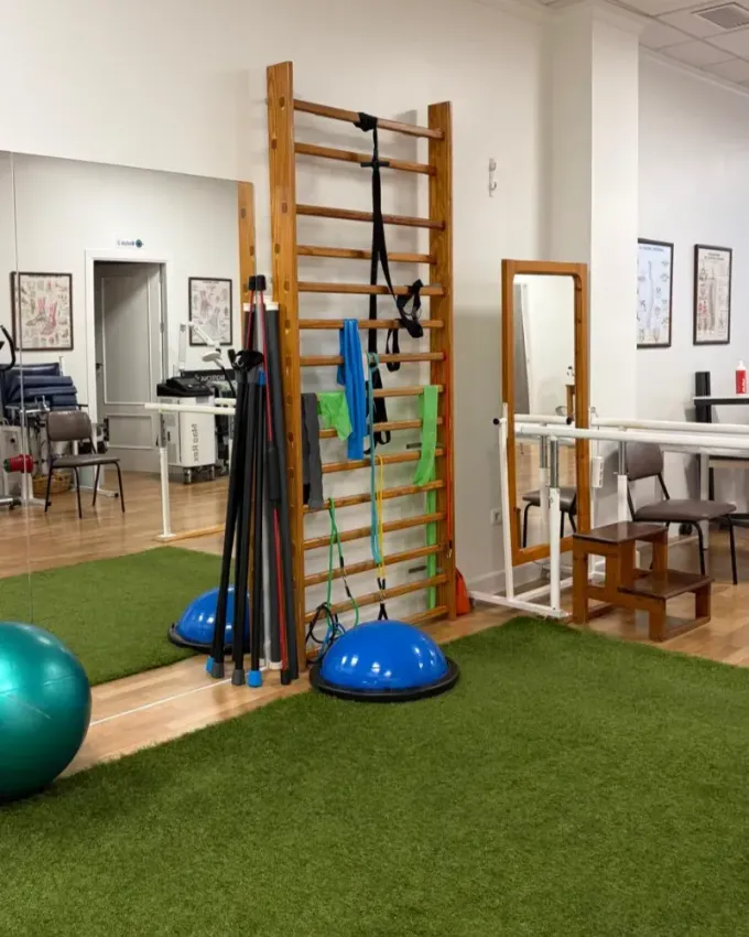 Sala de terapia luminosa con dos camillas de tratamiento, pelotas de ejercicio y estantes.