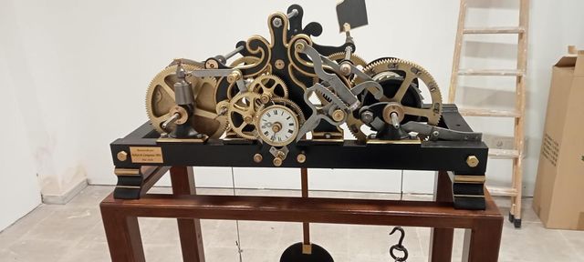 Engranaje mecánico antiguo sobre una mesa de madera en una habitación, con engranajes de latón y una esfera de reloj visible.