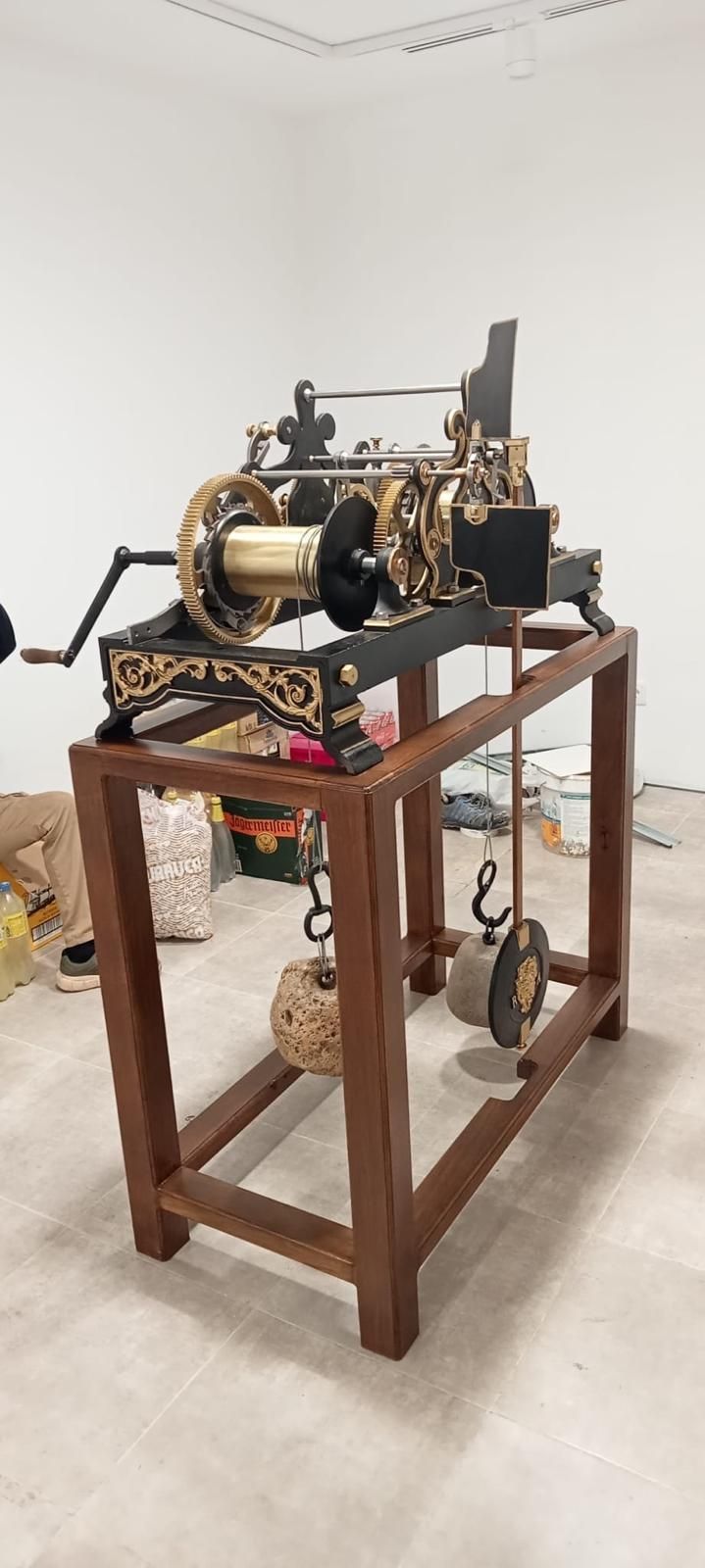 Una antigua máquina de metal negro sobre un soporte de madera en una sala de galería blanca.