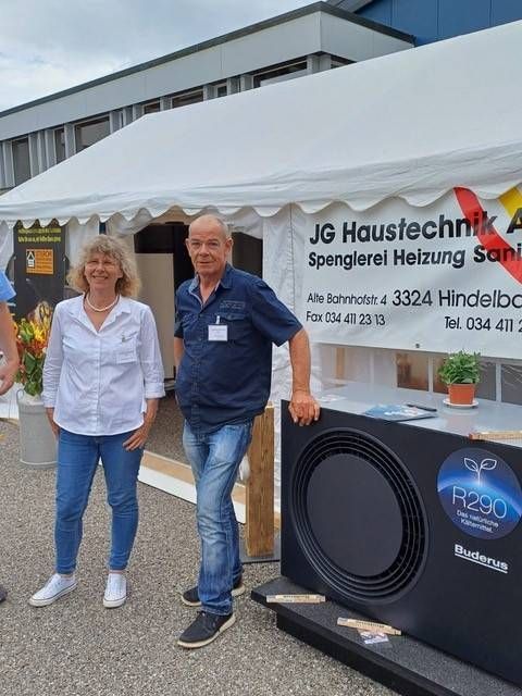 Zwei Personen stehen an einem Messestand unter einem weissen Zelt neben einem schwarzen Wärmepumpen-Display.