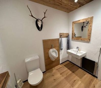 Modernes Badezimmer mit weisser Toilette, Wandurinal, Waschbecken, Spiegel und Hirschkopf-Wanddekoration