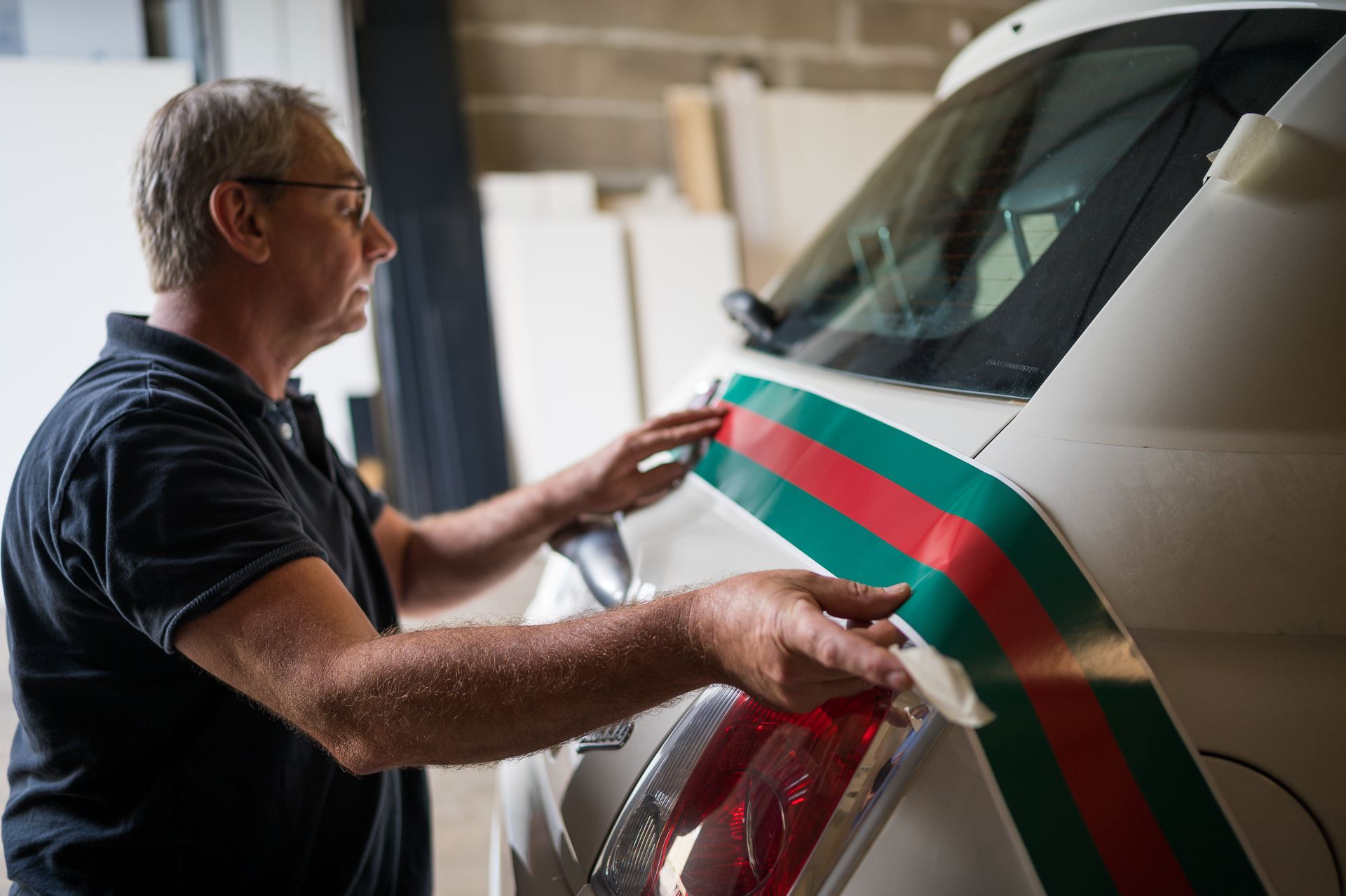 Un homme applique une bande décorative sur l'arrière d'un véhicule blanc dans un garage.