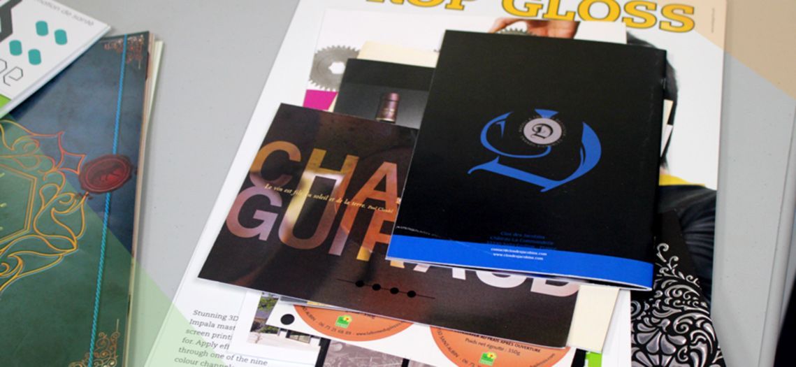 Pile de brochures noires avec des lettres dorées et bleues sur un magazine.