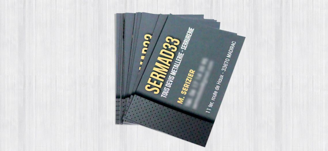 Pile de cartes de visite gris foncé avec lettrage doré sur fond clair imitation bois.
