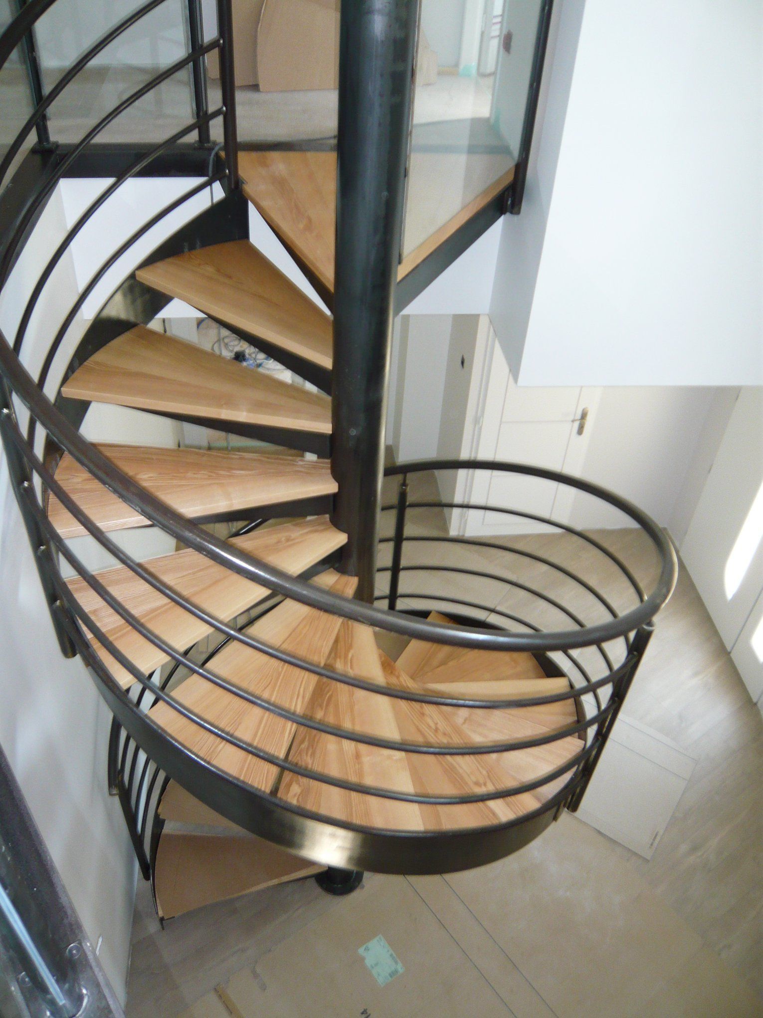 Escalier en colimaçon avec marches en bois et rampe en métal noir.