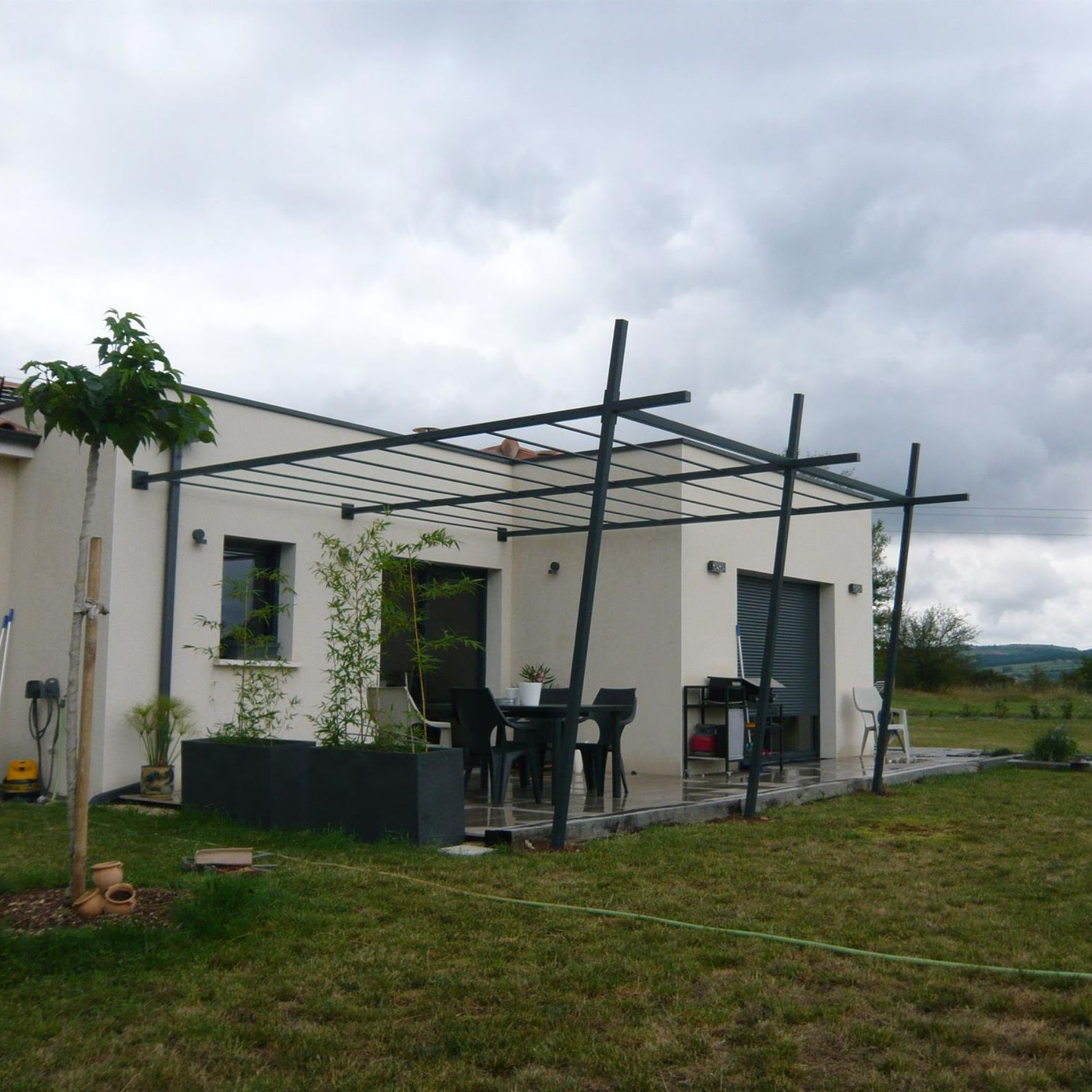 Maison blanche avec pergola noire au-dessus une terrasse extérieure.