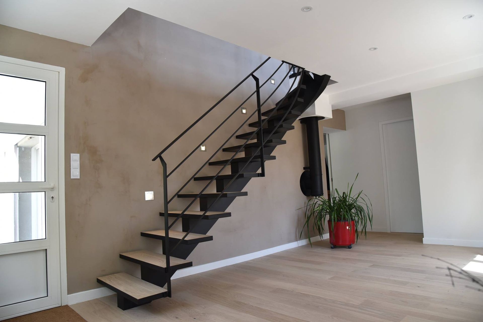 Escalier en métal noir avec marches en bois adossé à un mur brun.