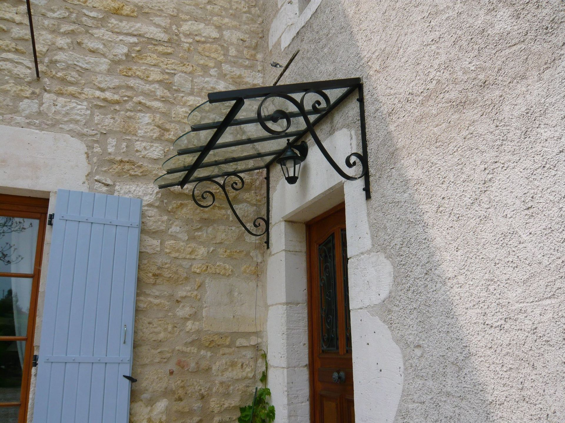 Auvent de porte en fer forgé recouvrant une porte en bois.