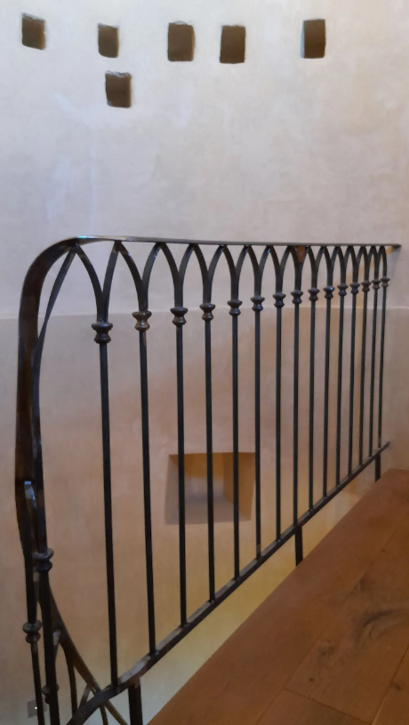 Rambarde en fer forgé à partie supérieure cintrée et barreaux verticaux.