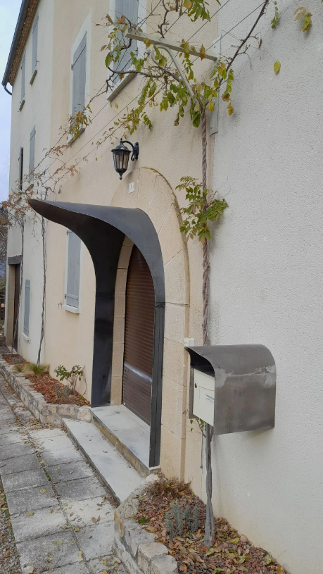 Bâtiment beige avec un auvent incurvé de couleur sombre au-dessus d'une porte marron.
