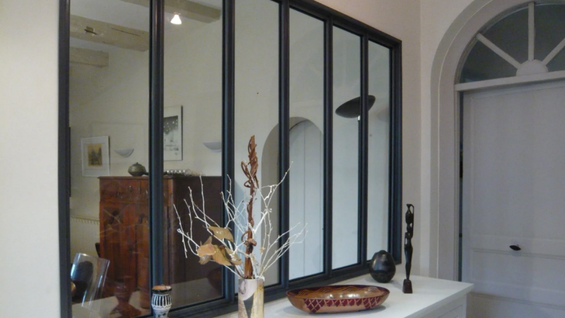 Une verrière à cadre noir, divisé en panneaux dans une entrée de maison.