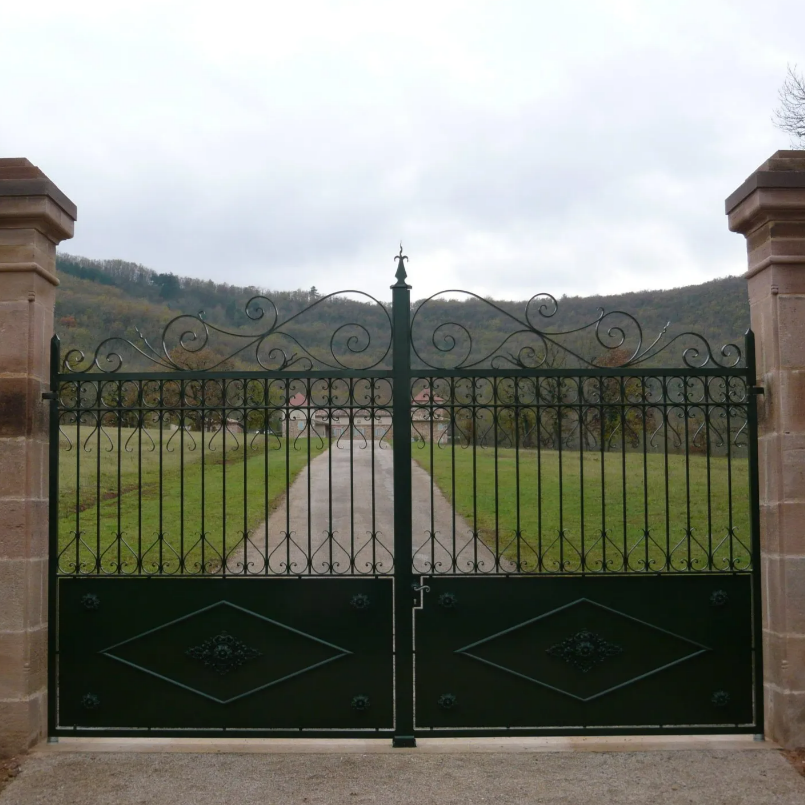 Portail en fer forgé vert, s'ouvrant sur une longue allée.