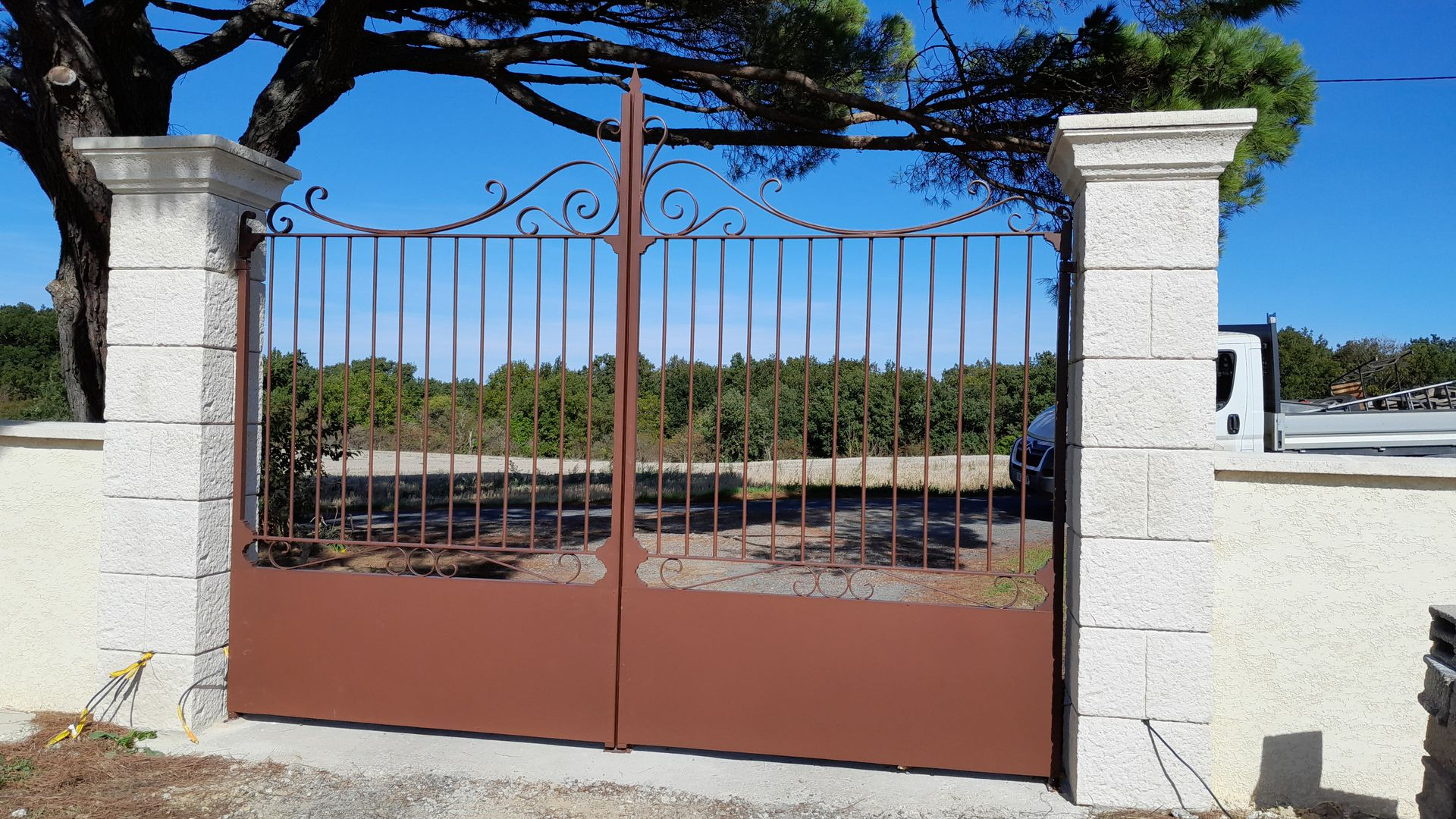 Portail en métal marron entre deux piliers de pierre.